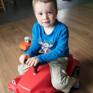 Un petit garçon est assis sur un petit tracteur rouge.