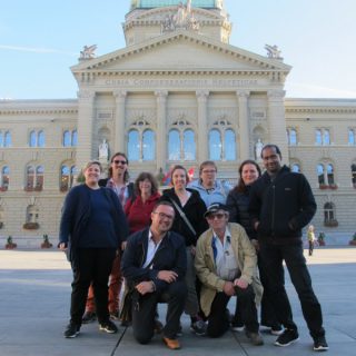 Un groupe d'hommes et de femmes devant le Palais fédéral à Berne.