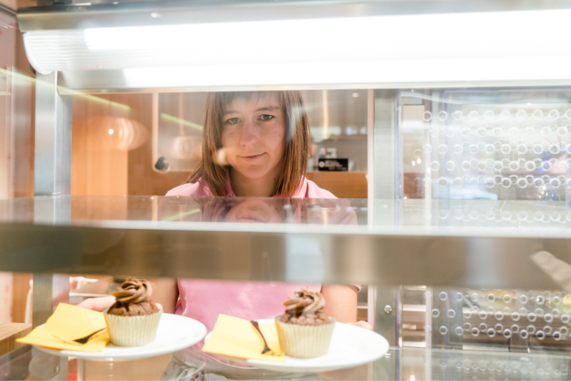 Eine junge Frau arrangiert Cupcakes in einem Schaufenster.