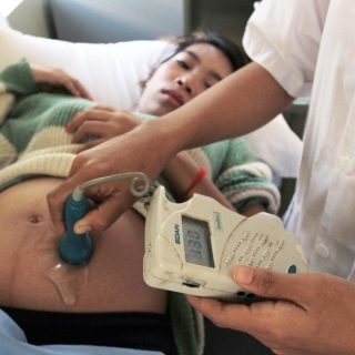 Eine Ärztin hält ein Messgerät auf den Bauch einer schwangeren Frau.