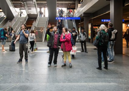 Deux jeunes se tiennent dans le hall d’une gare.