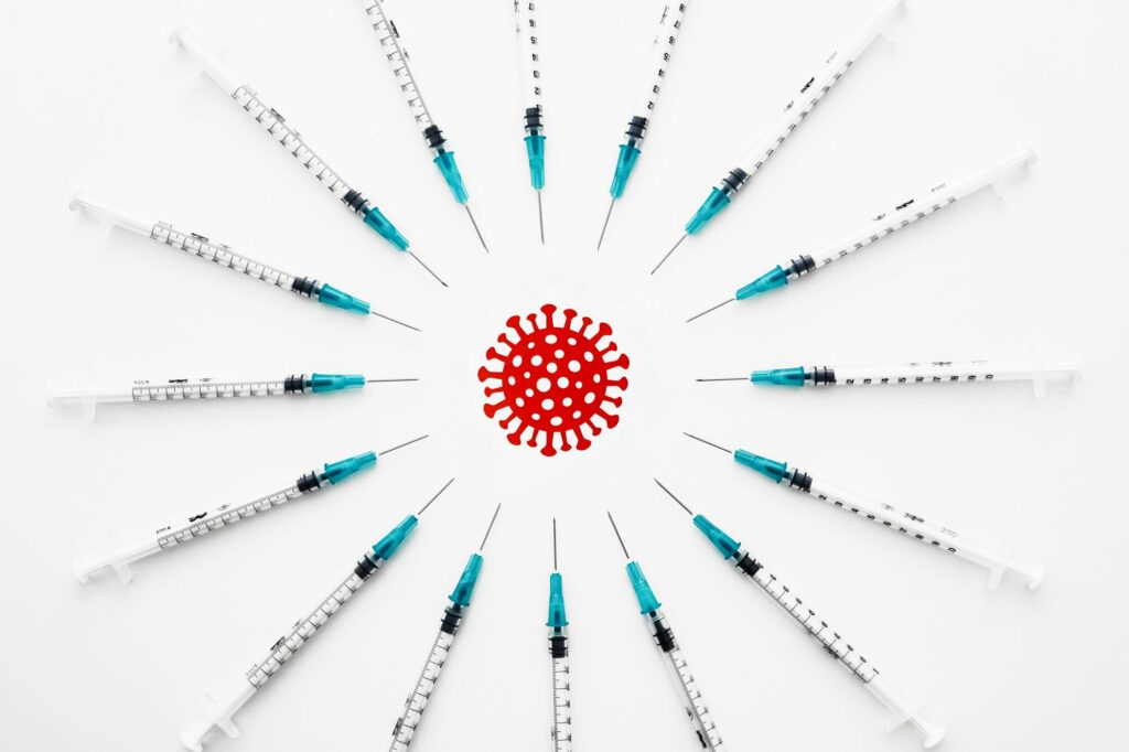 Des seringues posées en cercle pointent vers un virus dessiné au centre.