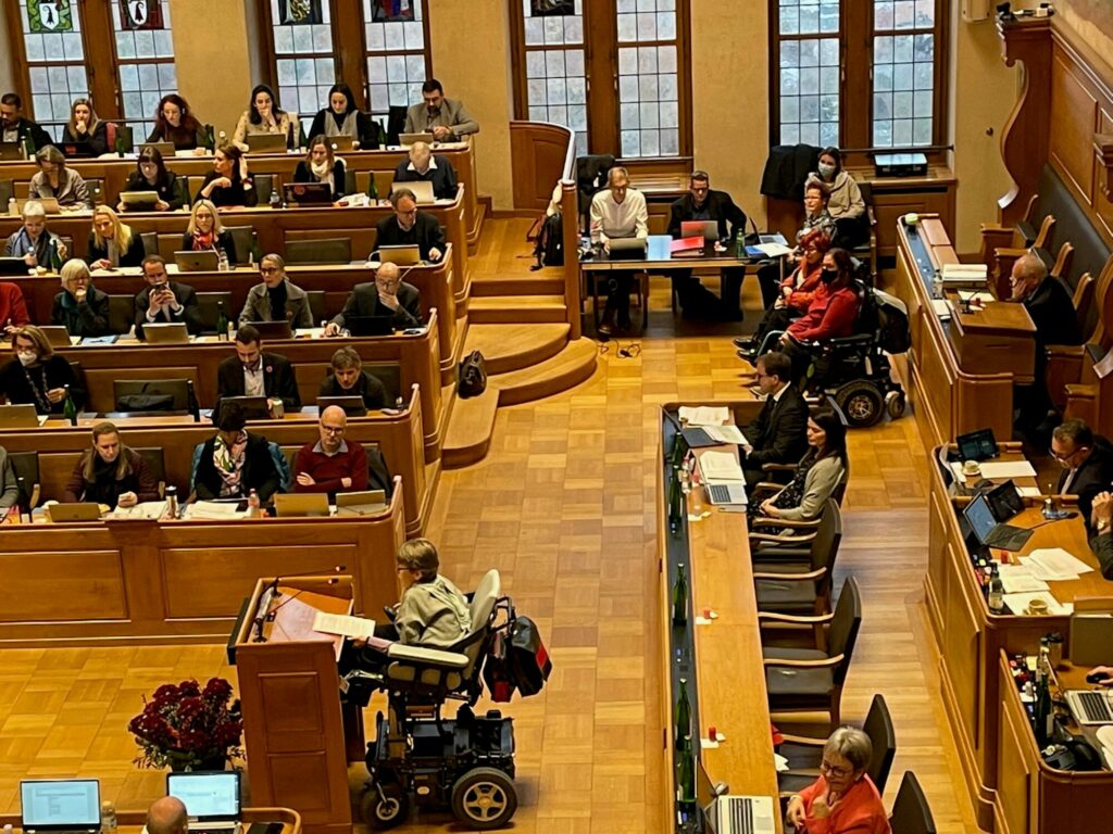 Une députée en fauteuil roulant parle devant les autres membres du Grand Conseil de Berne.