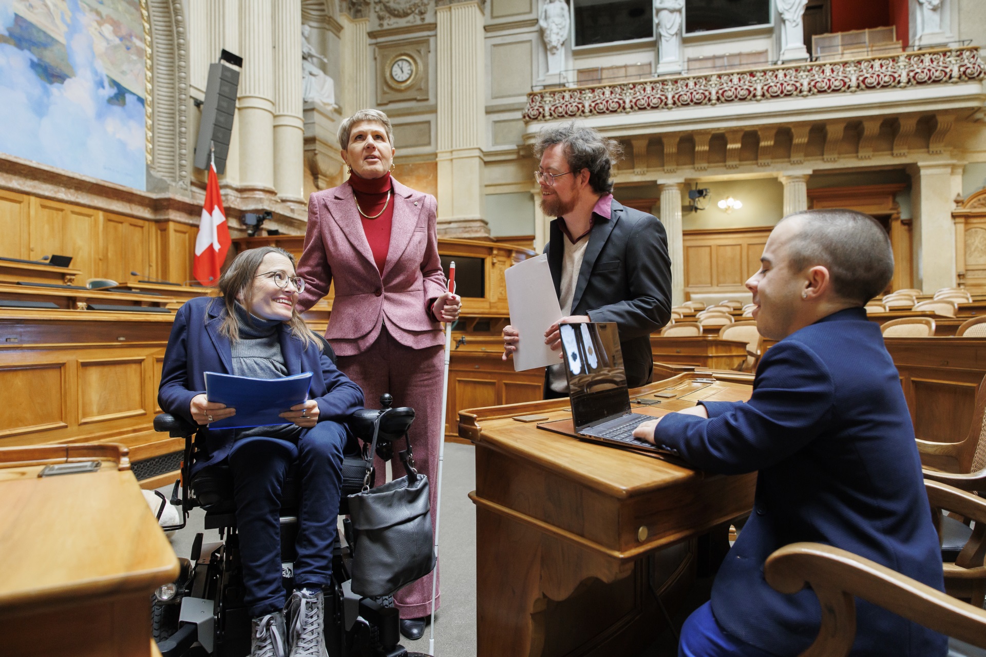 Deux femmes et deux hommes se trouvent dans le Palais fédéral, dont une femme en fauteuil roulant et une autre tenant une canne blanche d'aveugle.